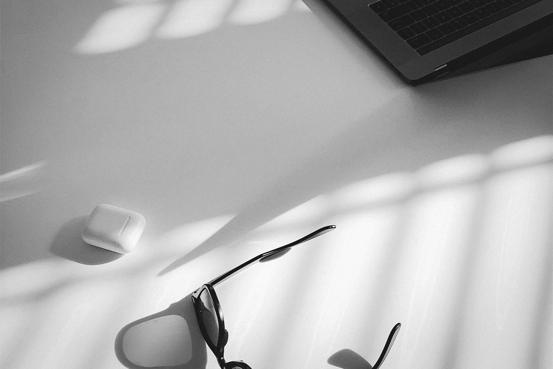 Airpods, eine Sonnenbrille und ein MacBook liegen auf einem Schreibtisch